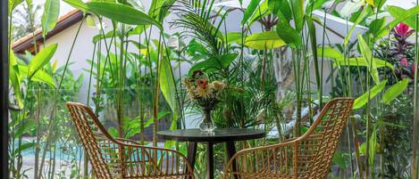 Un balcon avec des fauteuils en osier, une table et un vase de fleurs.