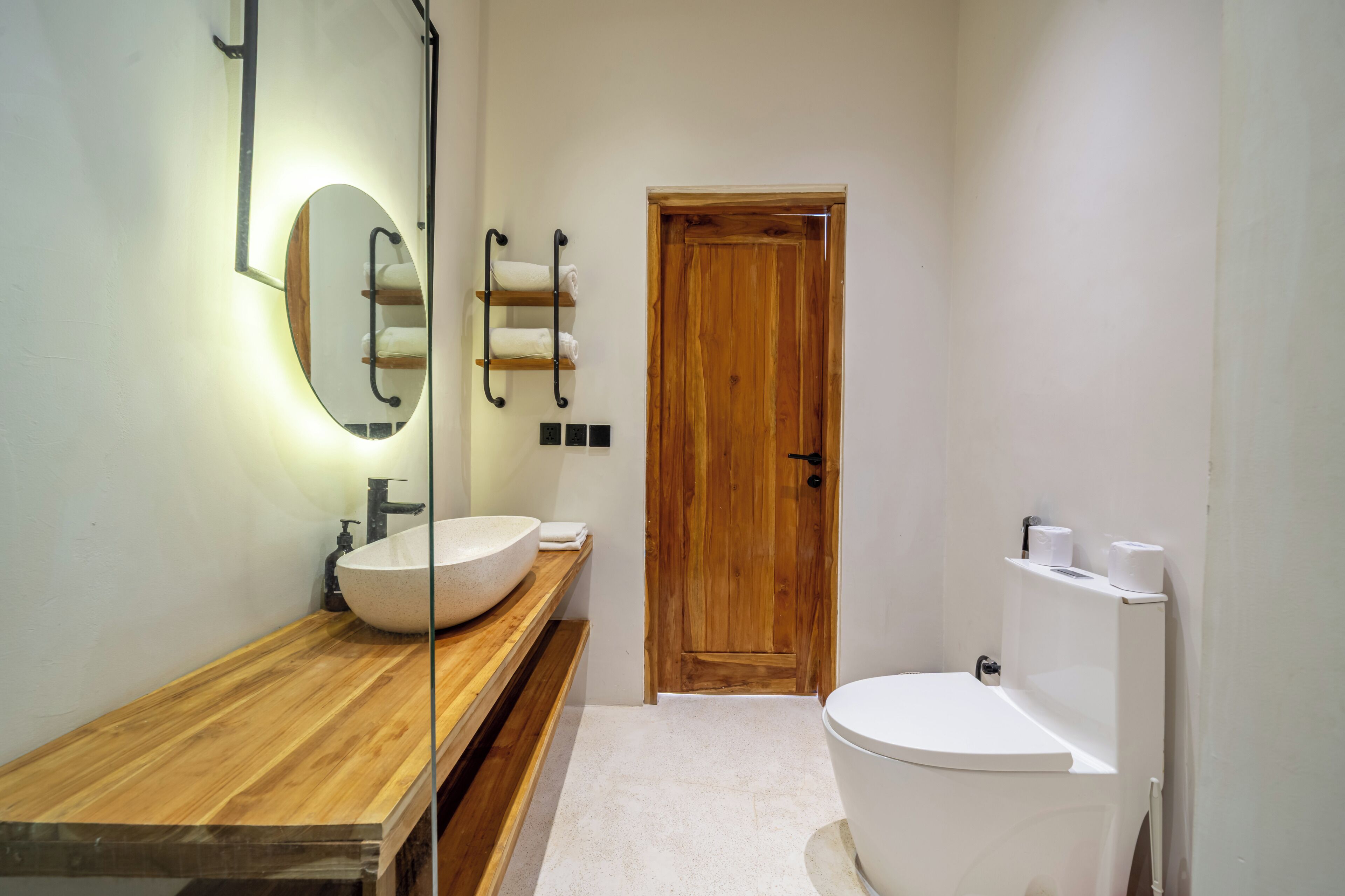 A bathroom with a wooden vanity, a large oval sink, a toilet, and a wooden door.