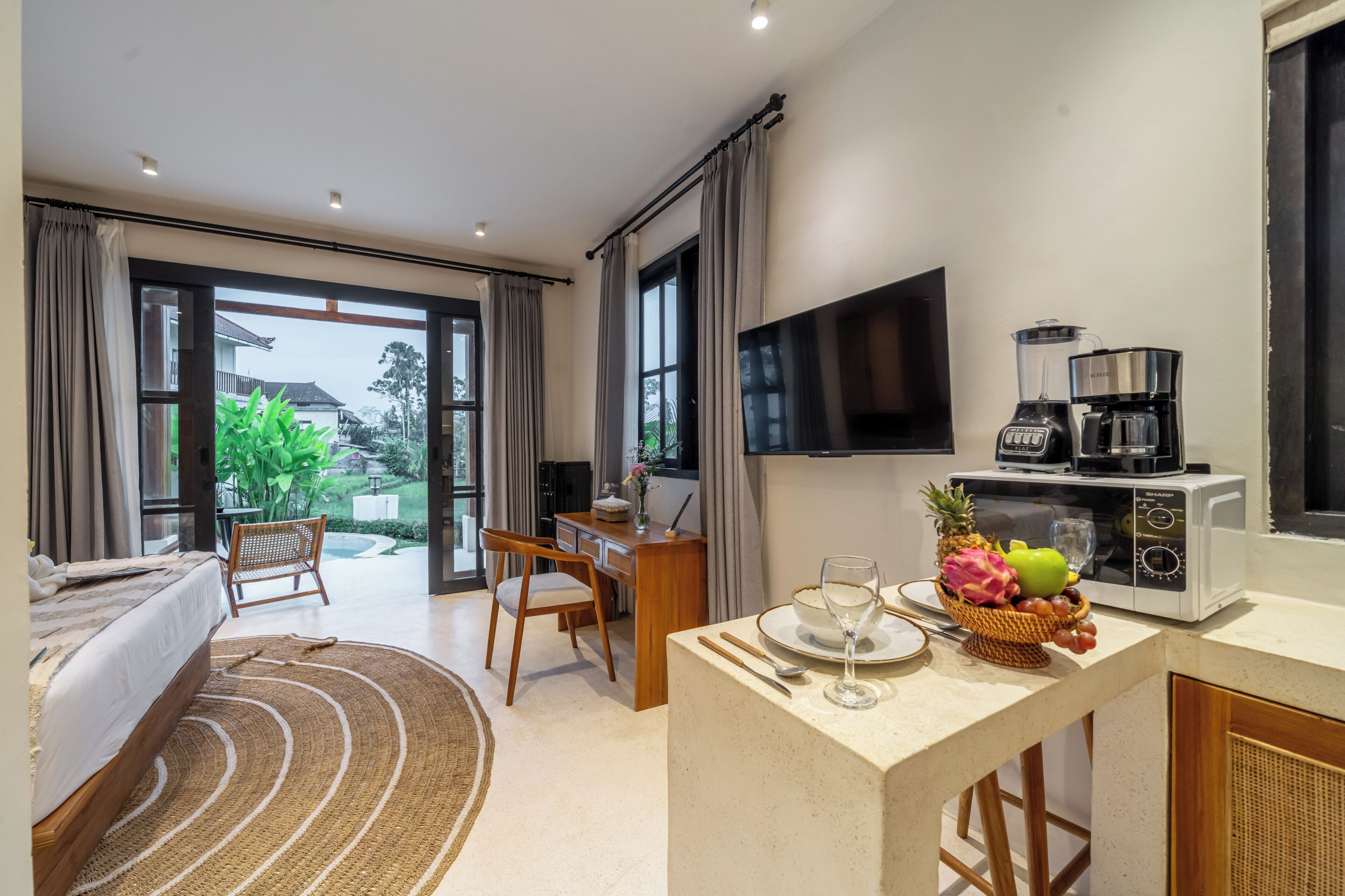A modern hotel room with a bed, a dining area, a kitchen with a microwave, and a TV.