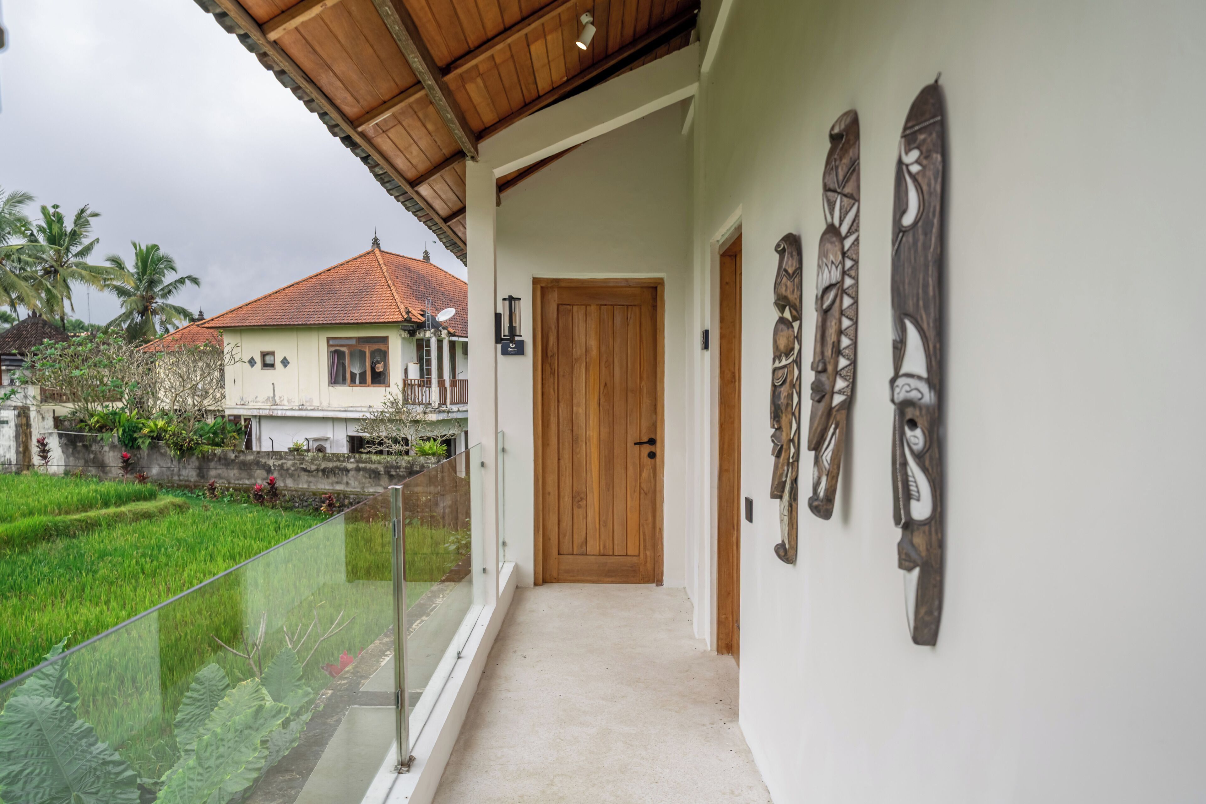 Un pasillo cubierto con una puerta de madera, baranda de cristal y decoración en las paredes.