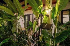 A room with large green plants, a wicker chair, and a sign indicating room number 2.