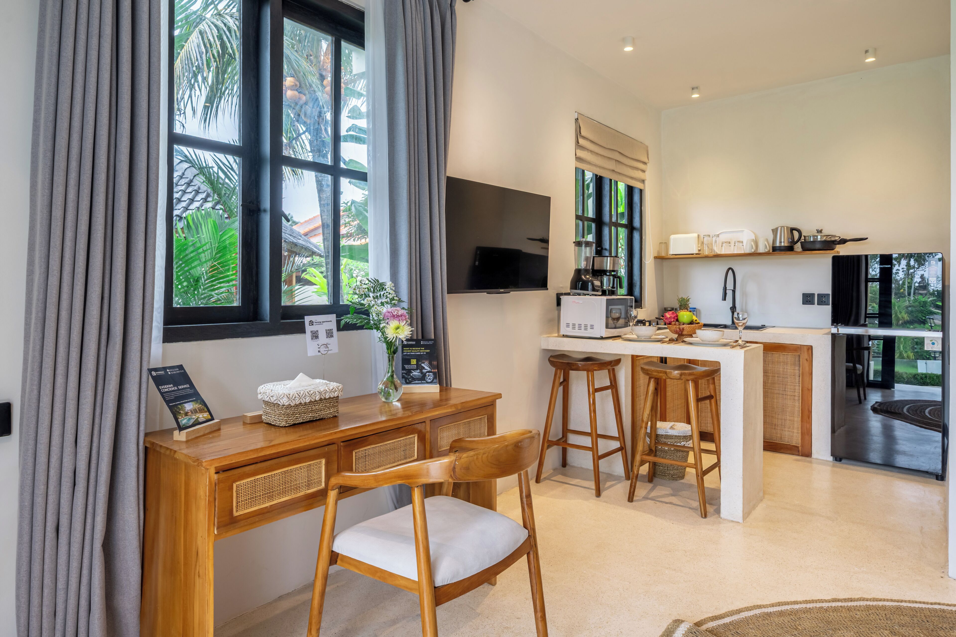 A modern kitchen with a central island, bar stools, a wooden dining table, and a TV mounted on the wall.