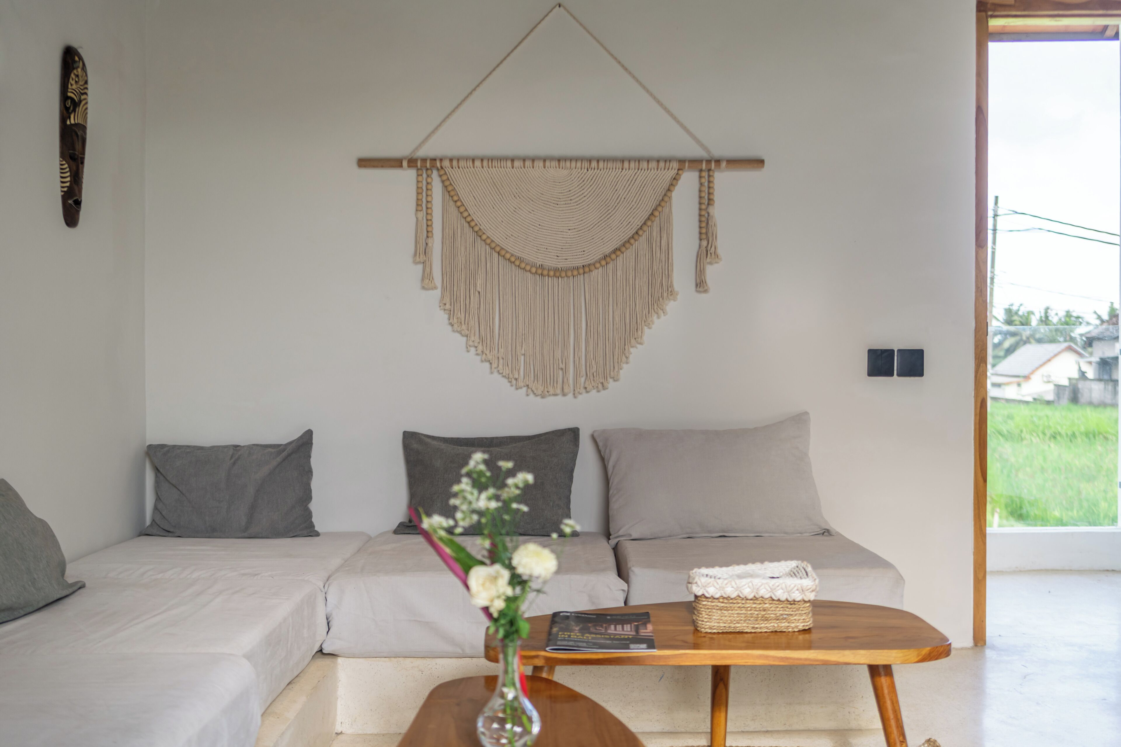 A minimalist living room with a sofa, a coffee table, and a macrame wall hanging.