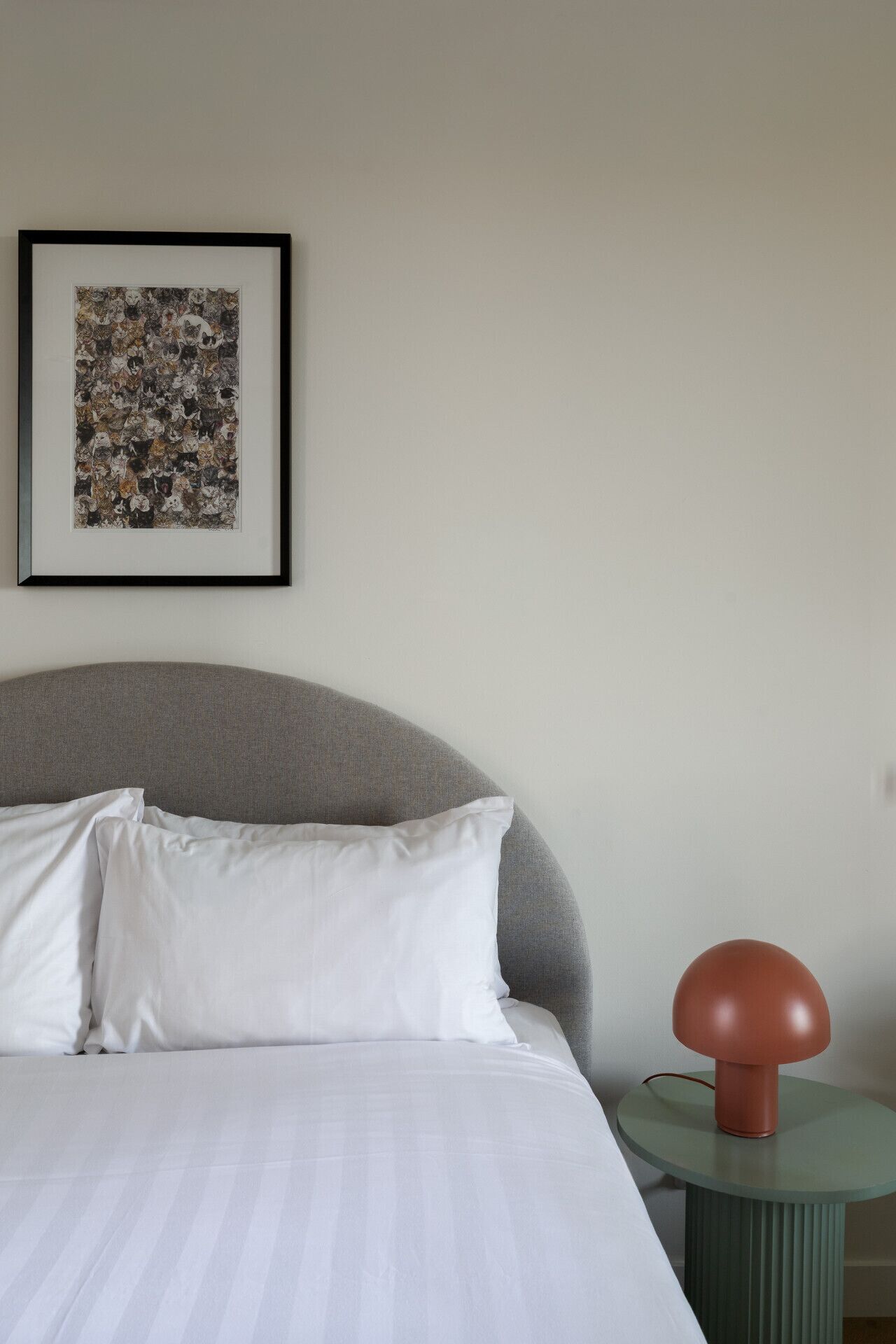 Una cama con sábanas blancas, cabecera gris y una obra enmarcada en la pared superior.