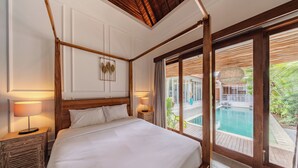A bedroom with a large bed, wooden headboard, bedside lamps, a view of a pool, and a sliding glass door. - Villa Naya Umalas (Kerobokan)