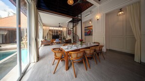 A dining area with a pool view, wooden chairs, a large dining table, and a staircase. - Villa Naya Umalas (Kerobokan)