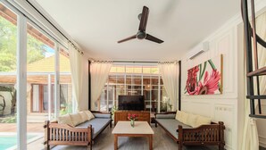 A living room with a TV, sofas, a coffee table, and a ceiling fan. - Villa Naya Umalas (Kerobokan)