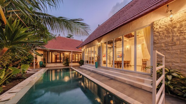 A swimming pool with a stone wall and glass doors leading to a dining area. - Villa Naya Umalas (Kerobokan)
