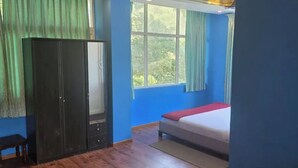 Una habitación con cama, armario, una mesita y ventana con cortinas.