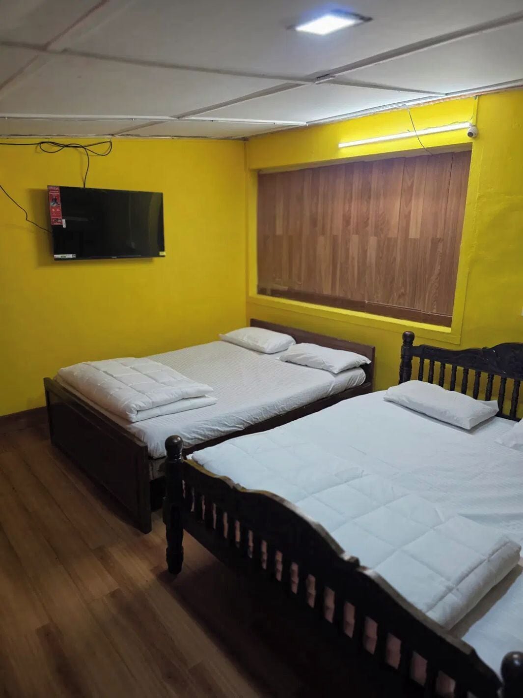 Een kamer met twee bedden, een televisie en een raam met zonwering.
