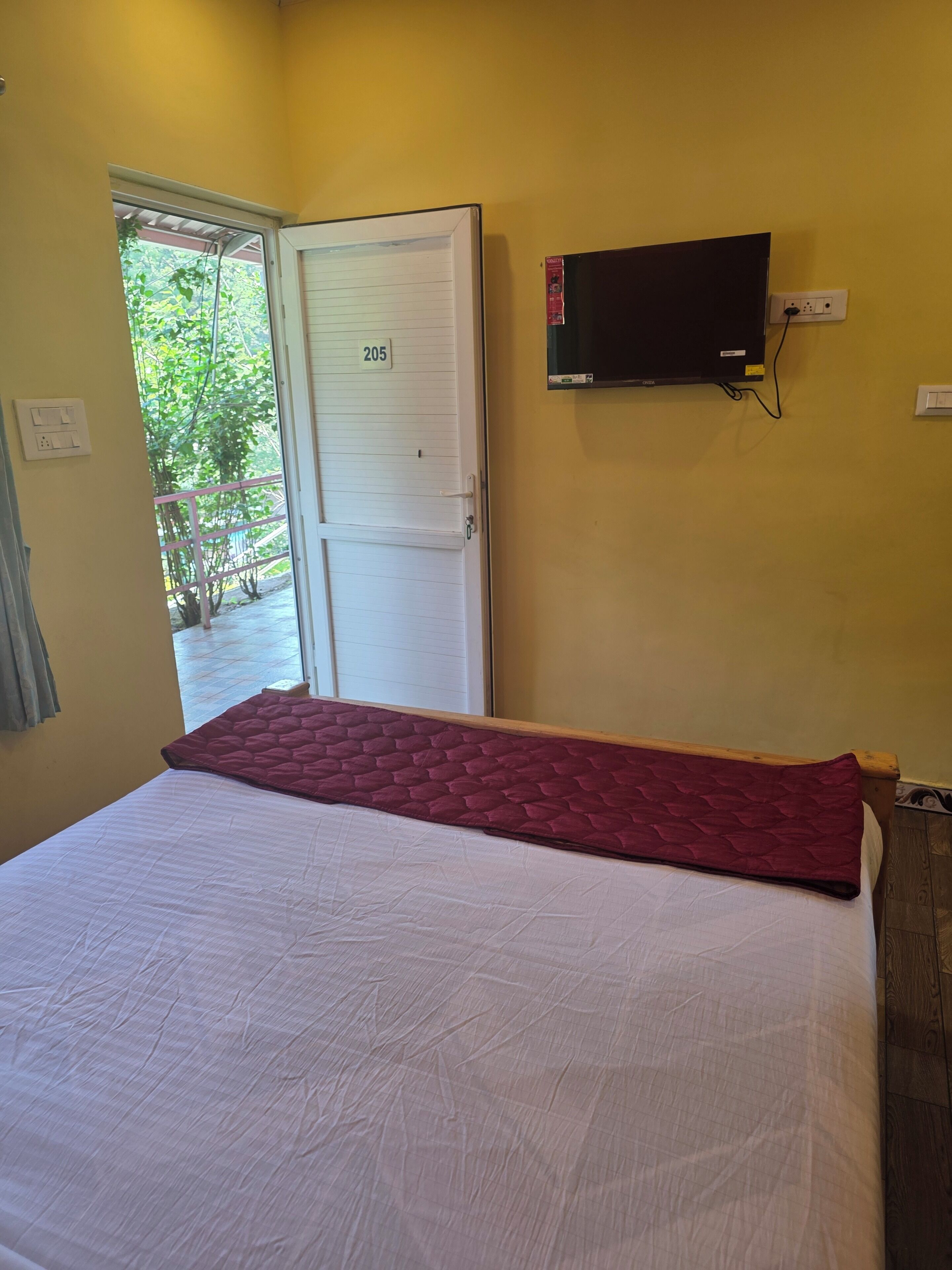 Een kamer met een bed, een aan de muur bevestigde televisie en een deur met een nummer.