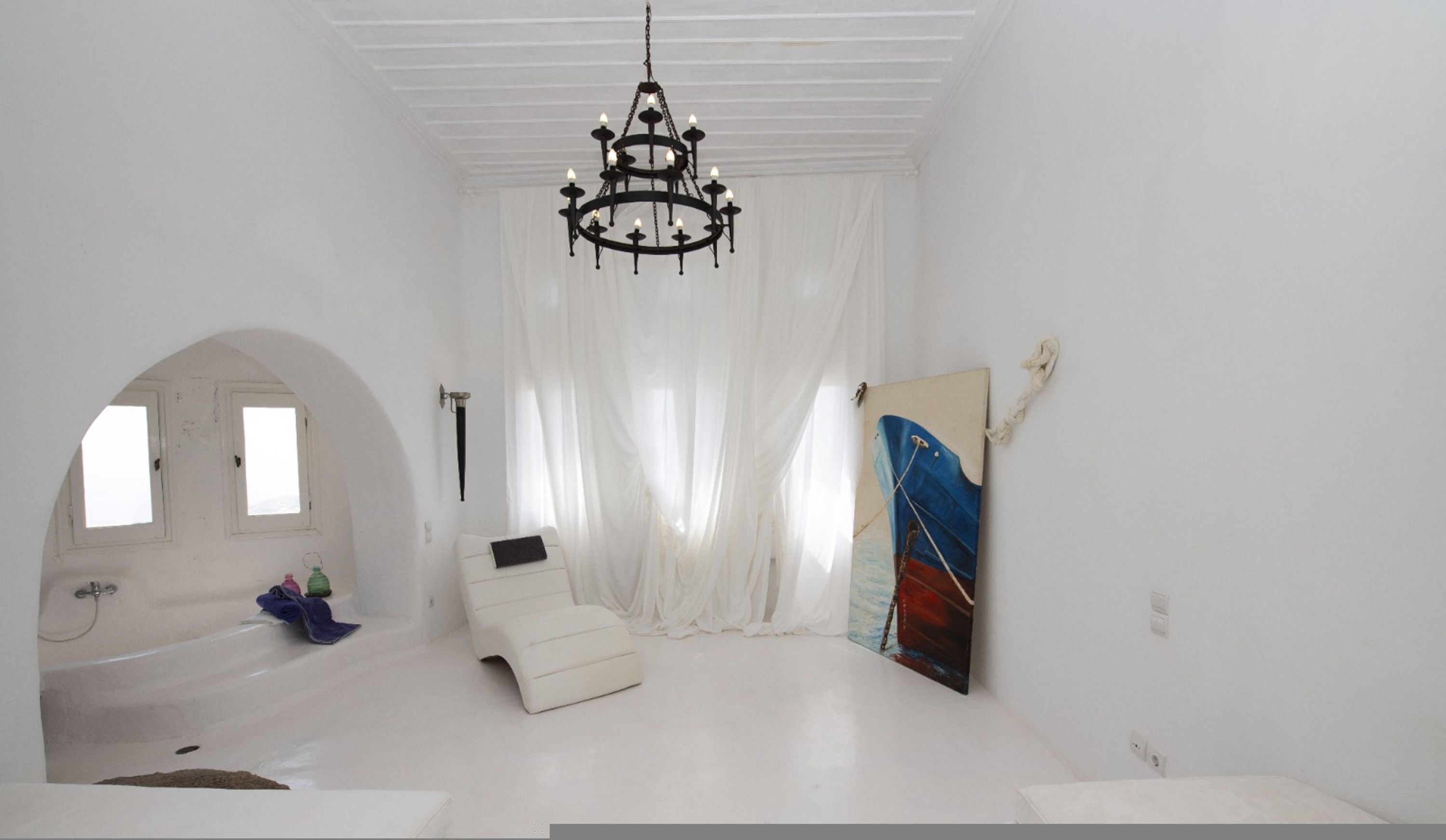 A room with a white color scheme, a chandelier, a bathtub, and a painting on the wall.