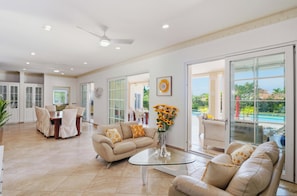 A spacious living area with a glass coffee table, beige sofas, a dining table with chairs, and a view of a swimming pool. - Fabulous 5-bedroom villa with AC, pool and beach access in charming Cabarete. (Cabarete)