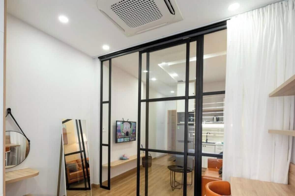 A modern room with a sliding glass door leading to a kitchen, a small seating area with a chair and table, and a shelf with a mirror.