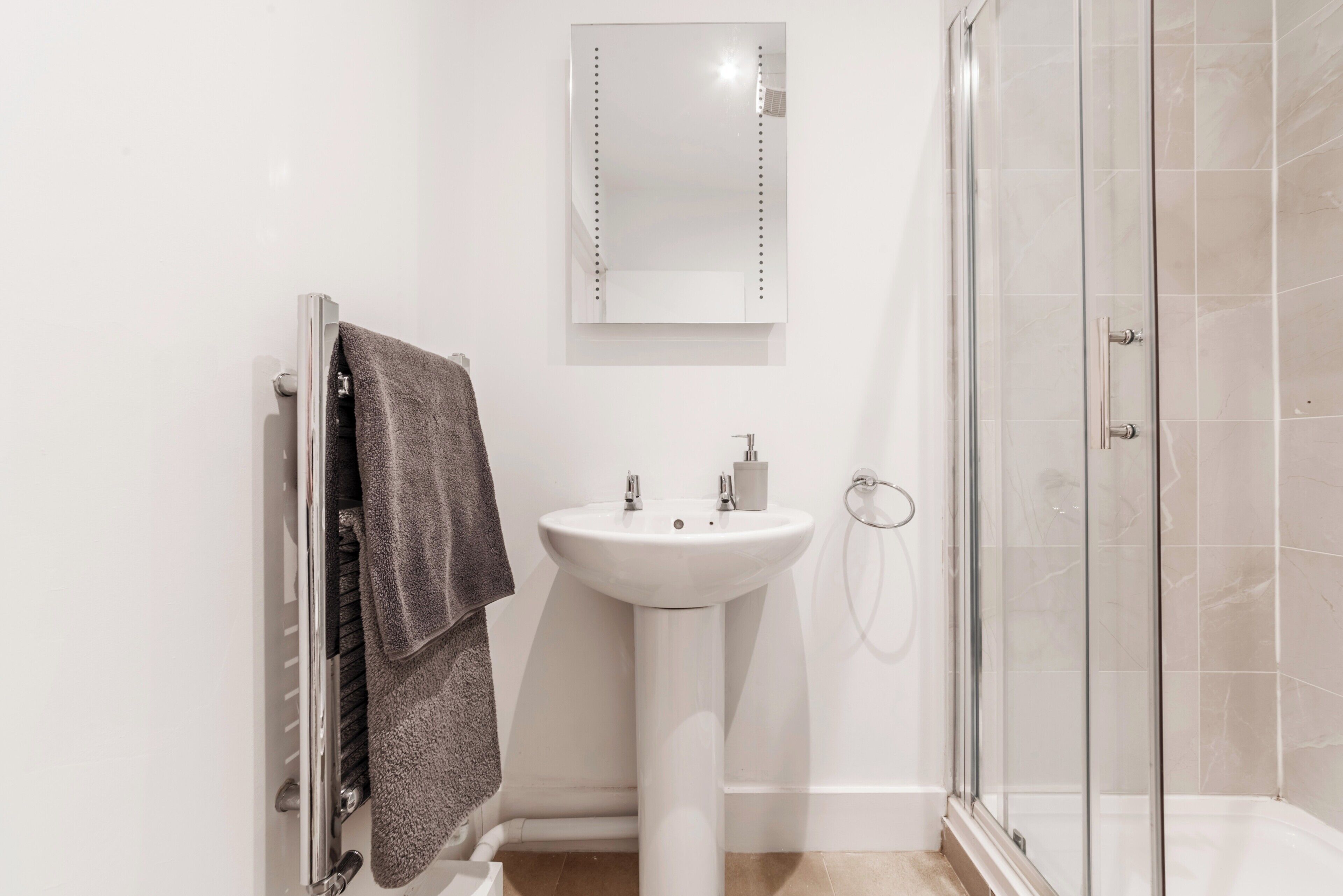 A bathroom with a white sink, a mirror, a towel rack, and a glass shower enclosure.