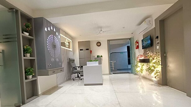 A modern reception area with a white reception desk, a grey wall with a decorative pattern, and a ceiling fan. - Hotel Royal Sky (Gandhinagar)