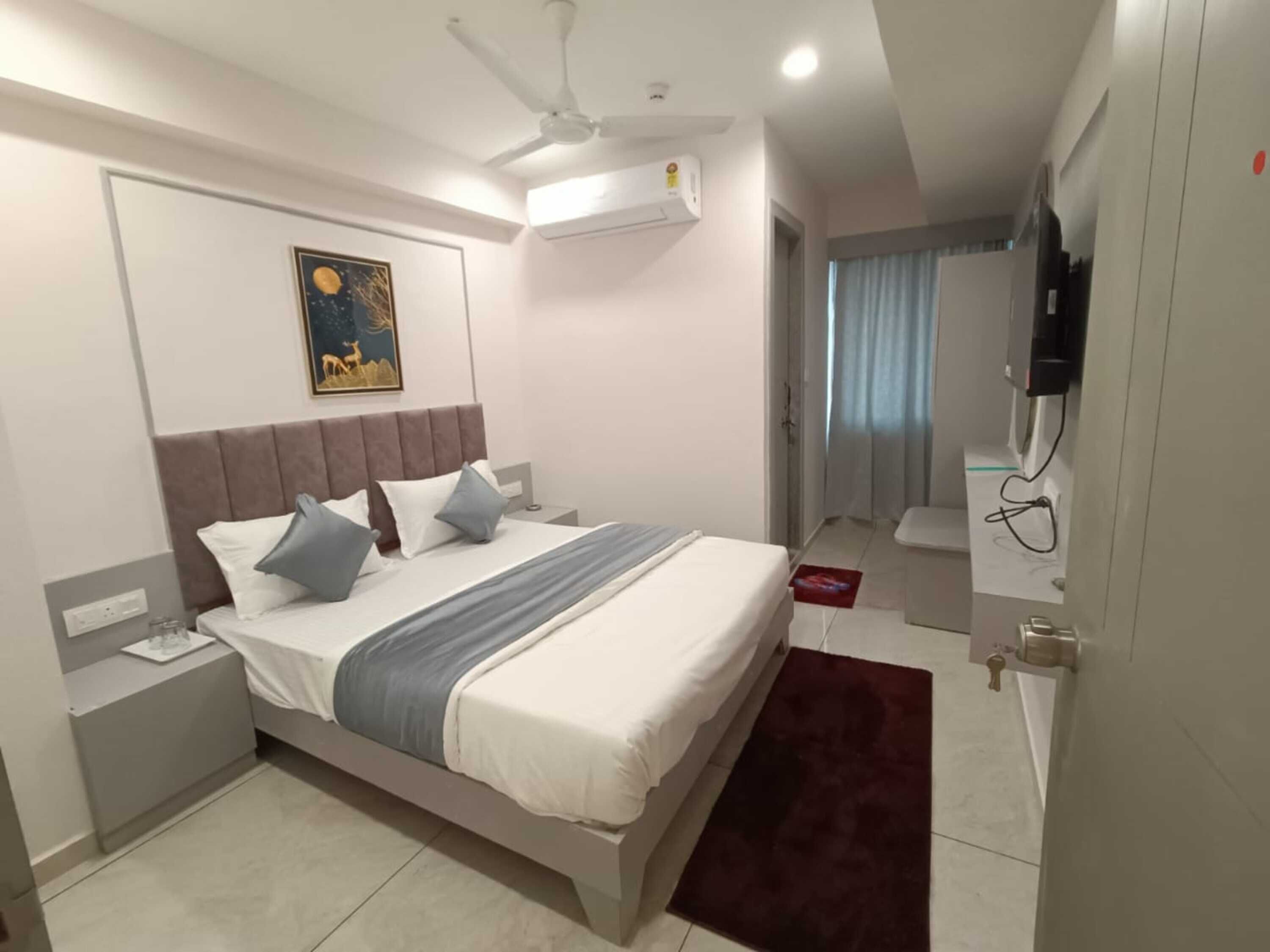 Una habitación de hotel moderna con una cama, mesita de noche, aire acondicionado y un cuadro en la pared.