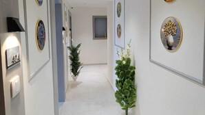 A hallway with framed artwork on the walls, a potted plant, and a number sign. - Hotel Royal Sky (Gandhinagar)