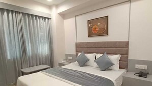 A modern hotel room with a large bed, bedside tables, a ceiling fan, and a painting on the wall. - Hotel Royal Sky (Gandhinagar)