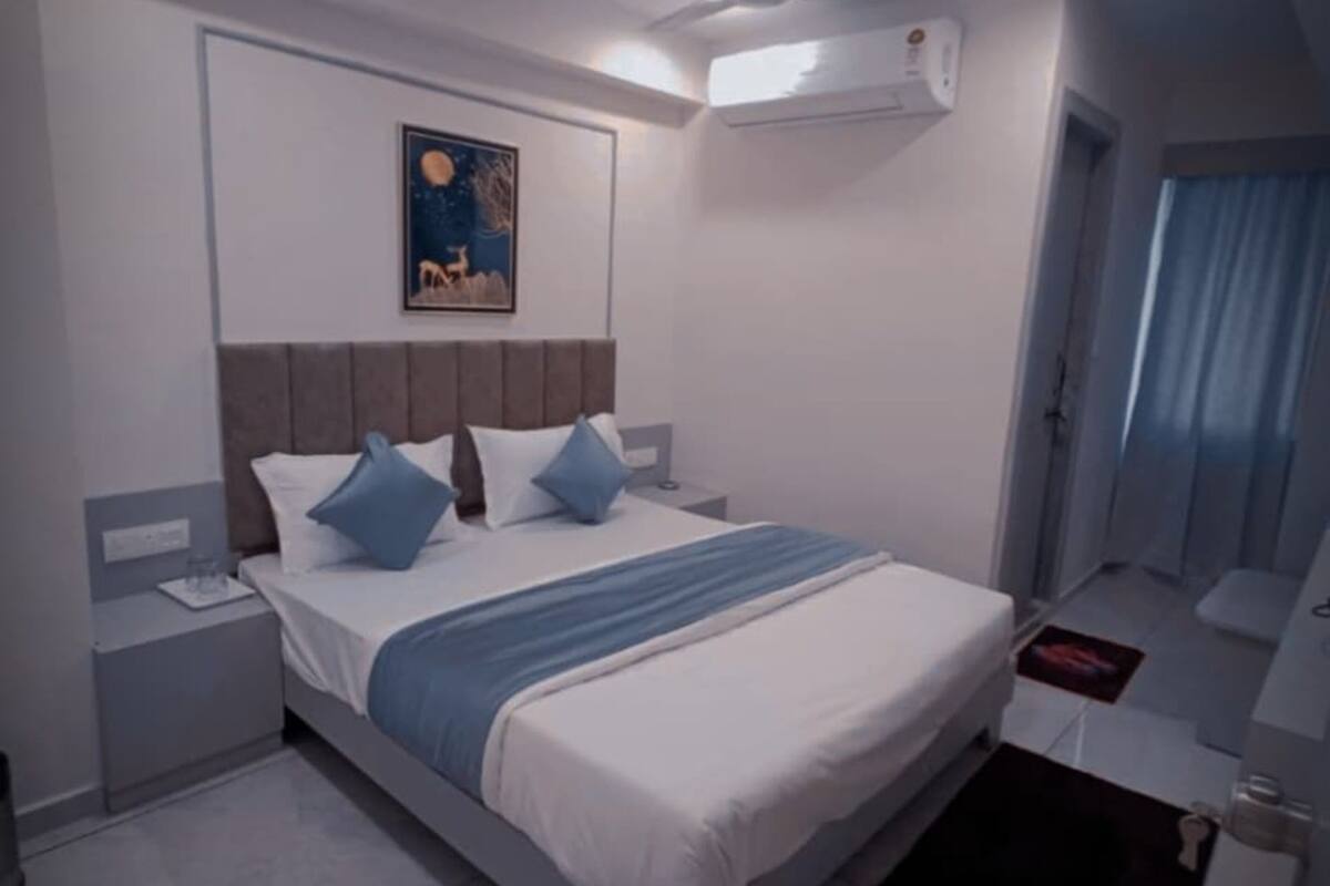 A modern hotel room with a bed, nightstands, a ceiling fan, an air conditioning unit, and a painting on the wall.