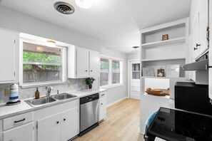 Una cucina moderna con mobili bianchi, lavastoviglie, fornello e una finestra con persiane.