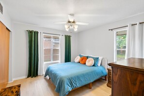 Ein Schlafzimmer mit einem Bett, einem Deckenventilator, einem Fenster mit Vorhängen und einer Holzkommode.