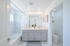 Ein modernes Badezimmer mit barrierefreier Dusche, einem Doppelwaschbecken mit großem Spiegel und einer Toilette.