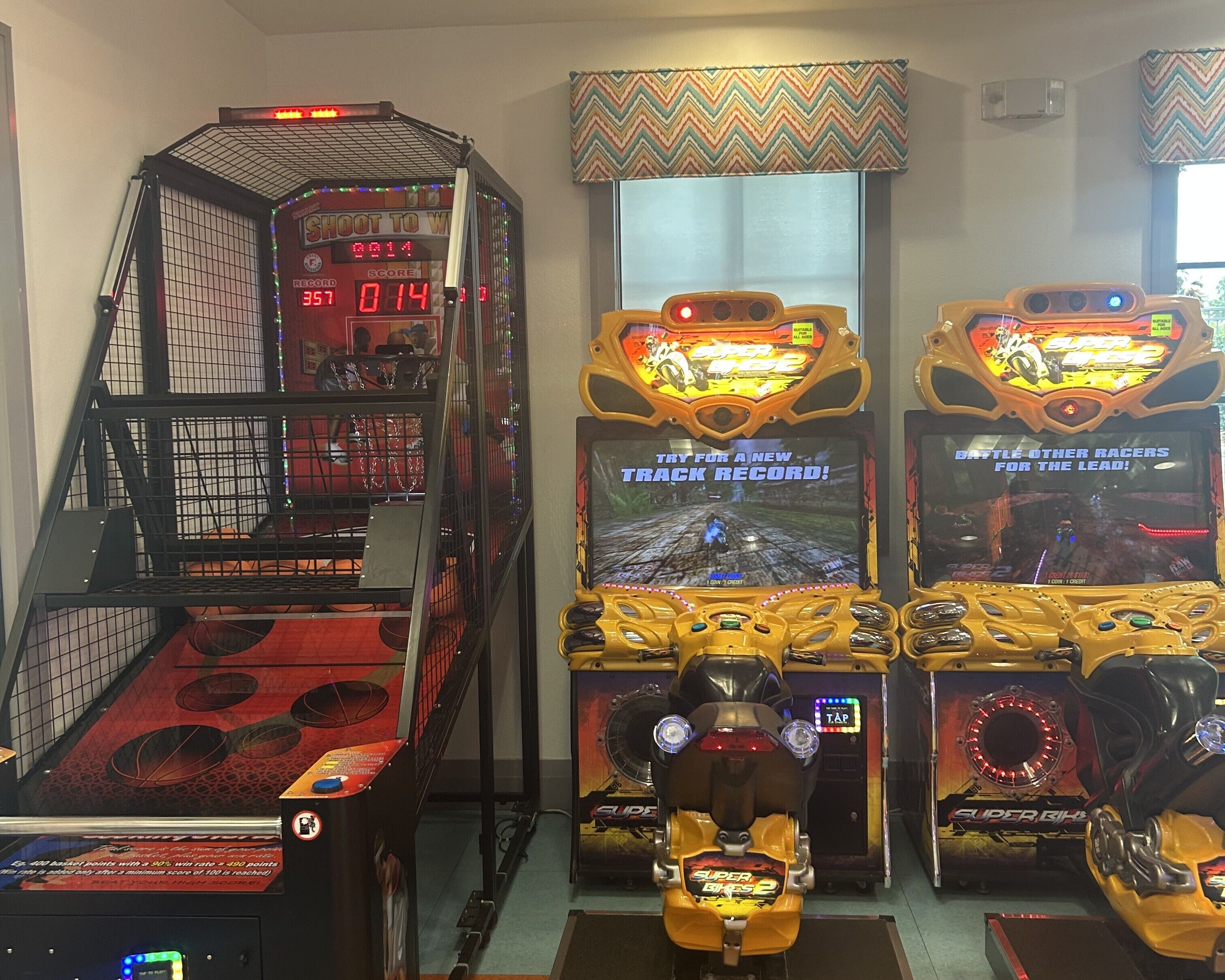 Un salón de juegos con máquinas de carreras, un juego de baloncesto y una pantalla de puntaje.