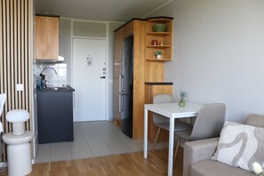 A compact kitchen with a refrigerator, stove, and sink, a dining table with chairs, and a sofa with a cushion.