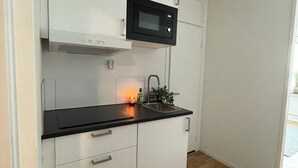 Una cocina con armarios blancos, una encimera negra, un microondas y un fregadero.