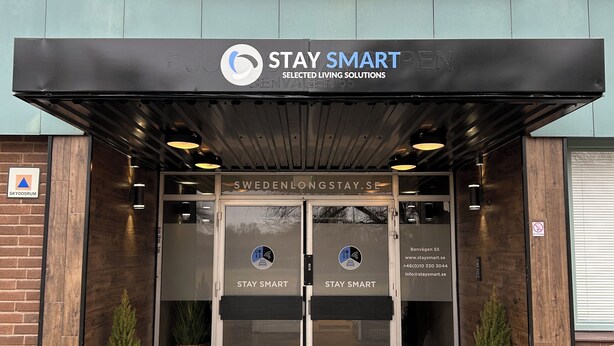 Entrada de un edificio con un letrero que dice 'STAY SMART SELECTED LIVING SOLUTIONS' y una dirección web 'SWEDENLONGSTAY.SE'.
