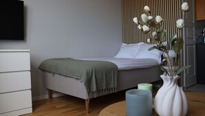 Un dormitorio con cama, mesita de noche y televisor montado en la pared.