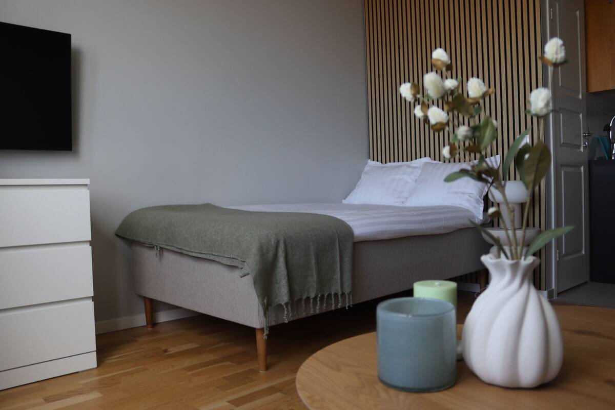 Un dormitorio con cama, mesita de noche y televisor montado en la pared.