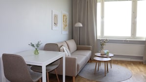 Una sala moderna con un sofá blanco, una mesa de comedor con sillas, una mesita auxiliar con un florero y una lámpara de pie.