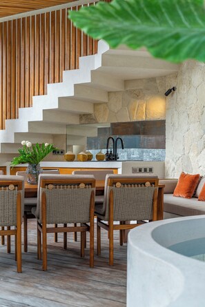Eine moderne Küche mit Steinrückwand, einer Holztreppe und einem Essbereich mit Korbstühlen und einem Tisch.