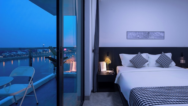 Habitación de hotel con balcón, cama con ropa de cama a cuadros, mesita de noche con lámpara y un mapa enmarcado en la pared.