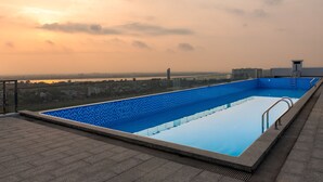 Una piscina en la azotea con vistas despejadas del paisaje urbano y una puesta de sol al fondo.