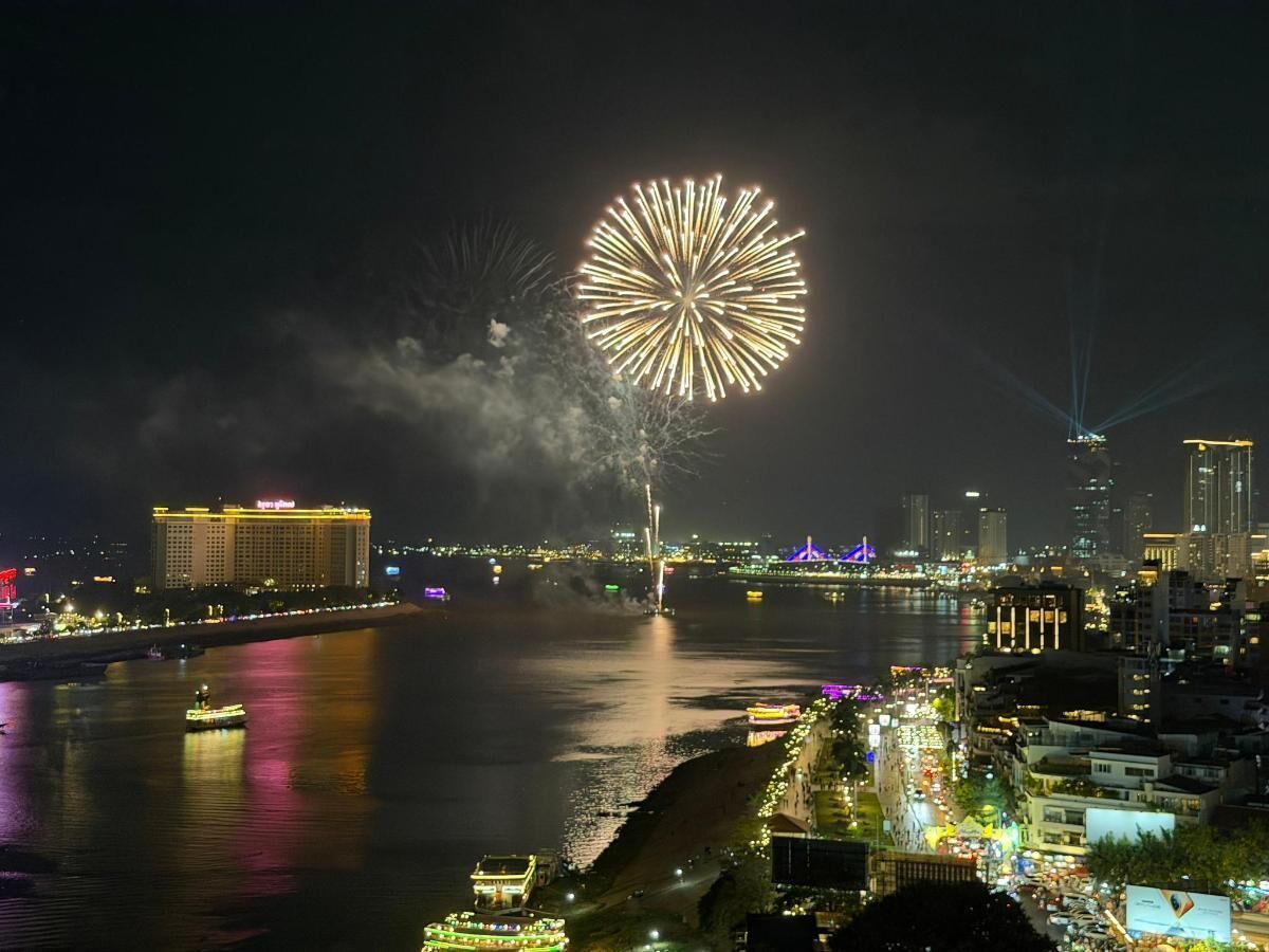 A cityscape with a river, a large illuminated building, and fireworks in the sky.