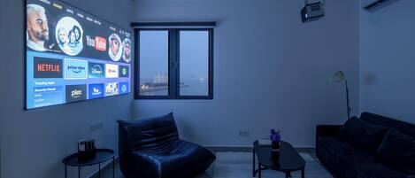 Een moderne woonkamer met een grote tv waarop streamingdiensten worden afgespeeld, een leren bank, een salontafel en een uitzicht op een stadsgezicht door een raam.