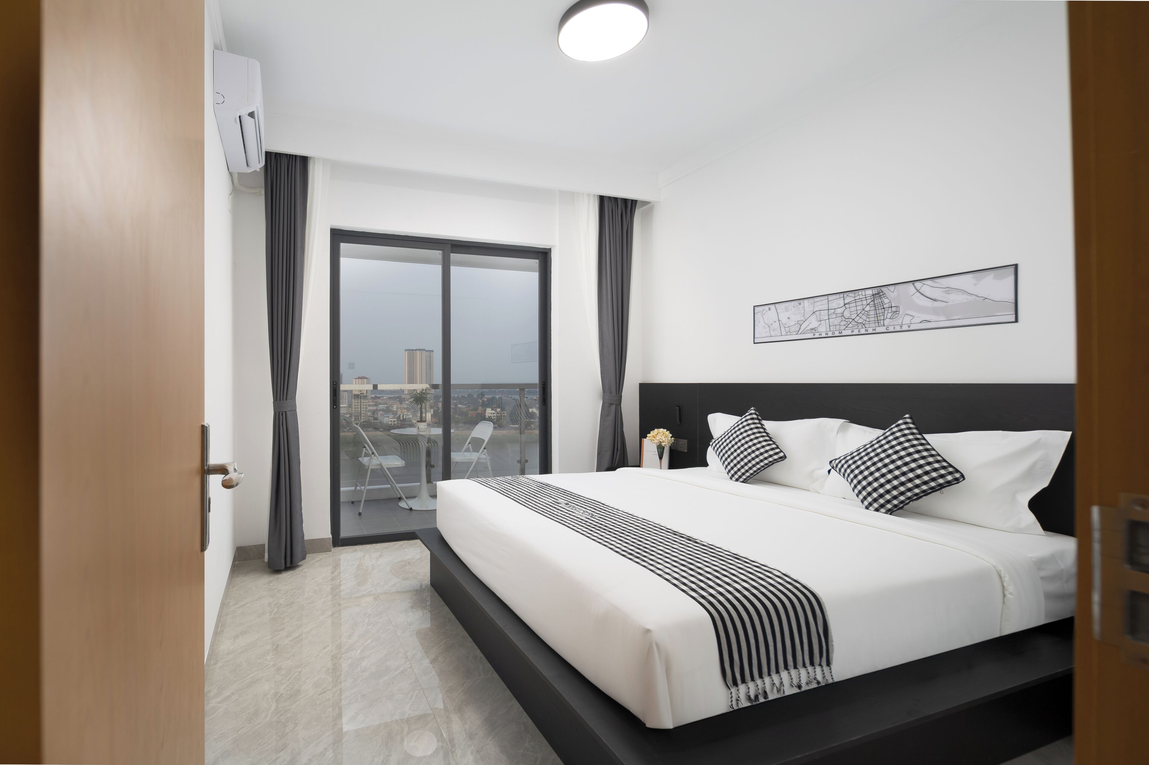 A modern hotel room with a large bed, a view through a sliding door, a ceiling light, and a framed artwork on the wall.