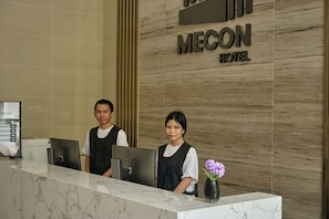 A hotel reception desk with a marble counter, two receptionists, and a sign for the Mecon Hotel. - Mecon Hotel (Phnom Penh)