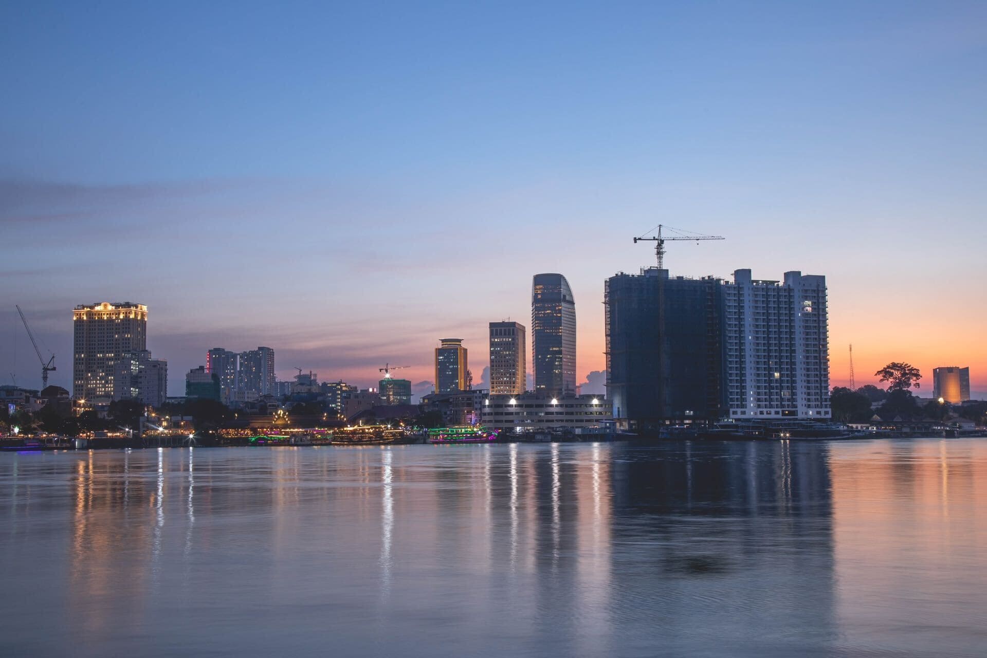 Une vue sur les grat-ciel d’une ville, avec une étendue d’eau reflétant les bâtiments et un coucher de soleil en arrière-plan.