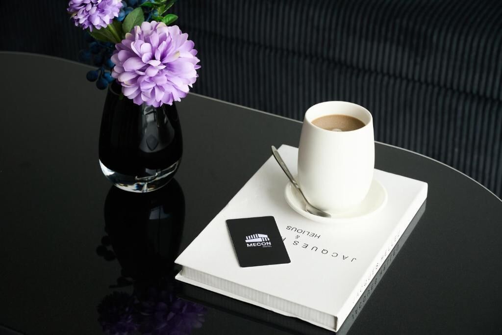 A black table with a white cup of coffee, a black card, and a book titled 'JACQUES HENLOUS' with a black card on top.