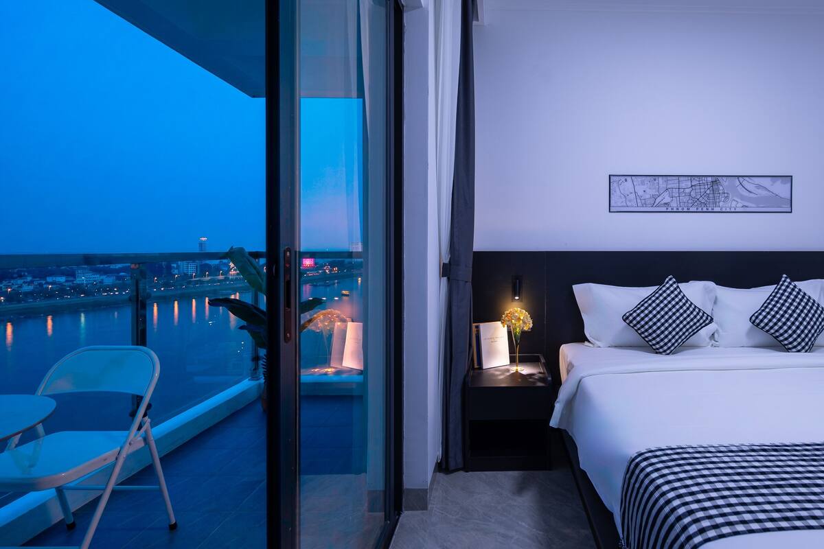 A hotel room with a balcony, a bed with black and white checkered bedding, a nightstand with a lamp, and a framed map on the wall.