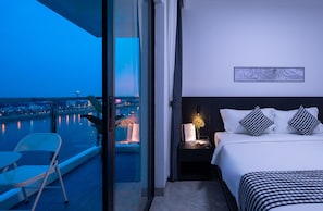 Quarto de hotel com varanda, cama com roupa de cama em padrão xadrez preto e branco, mesa de cabeceira com abajur e um mapa emoldurado na parede.