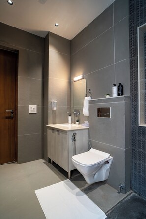 A modern bathroom with a toilet, sink, and mirror. - Alaya Stays Udgam Vilas 3-BHK With Lift (Dehradun)