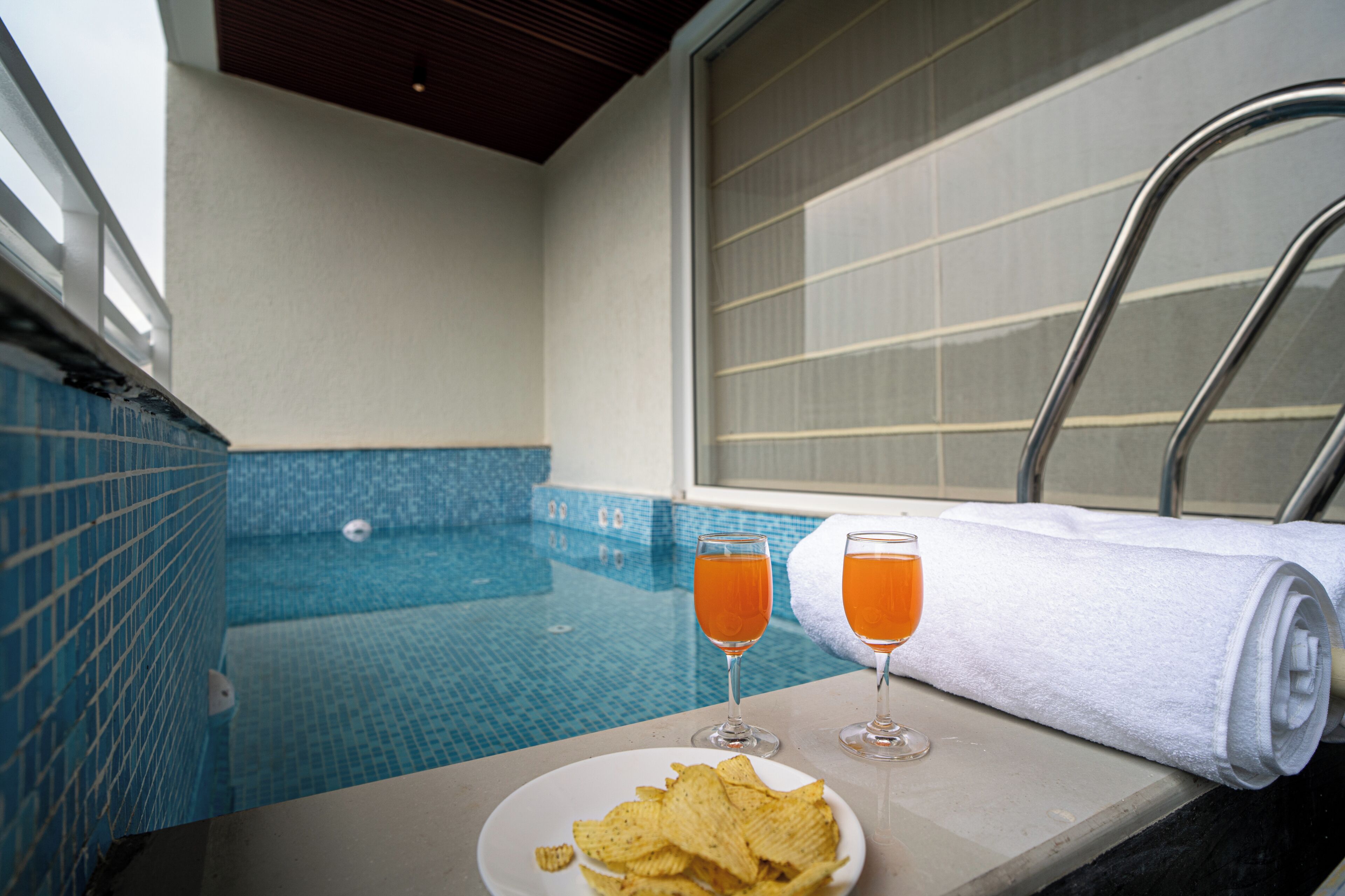A poolside area with a glass of orange drink, a plate of chips, and a rolled towel.