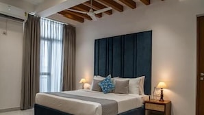 A modern bedroom with a large bed, wooden beams, a dark headboard, bedside lamps, and a patterned rug. - Alaya Stays Udgam Vilas 3-BHK With Lift (Dehradun)