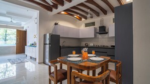 A modern kitchen with white cabinets, a black range hood, and a dining area with a wooden table and chairs. - Alaya Stays Udgam Vilas 3-BHK With Lift (Dehradun)