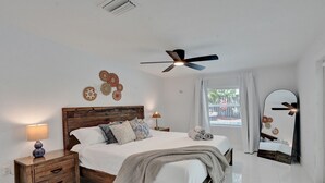A bedroom with a wooden bed, bedside lamps, a ceiling fan, a large window with curtains, and a wall mirror.